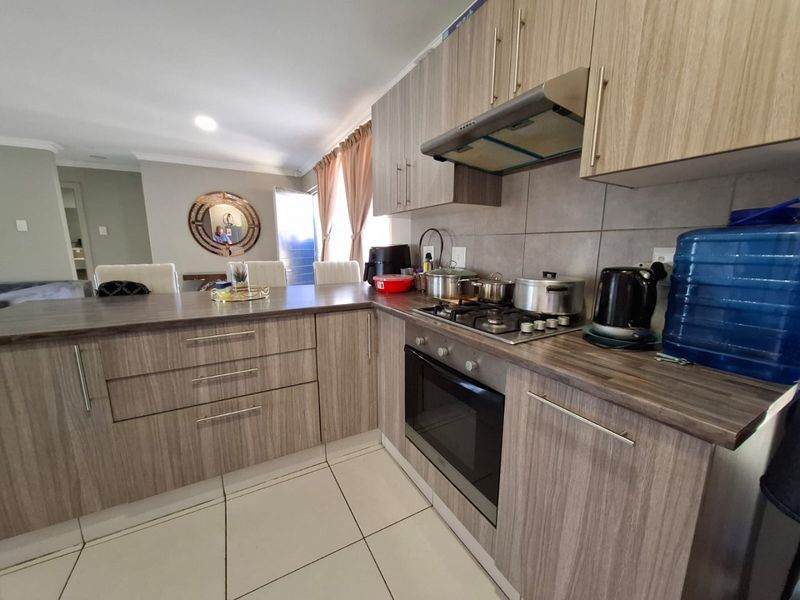 Open-plan kitchen featuring modern wood-look cabinetry, laminate countertops, a gas hob, built-in oven, and a breakfast bar overlooking the living area.