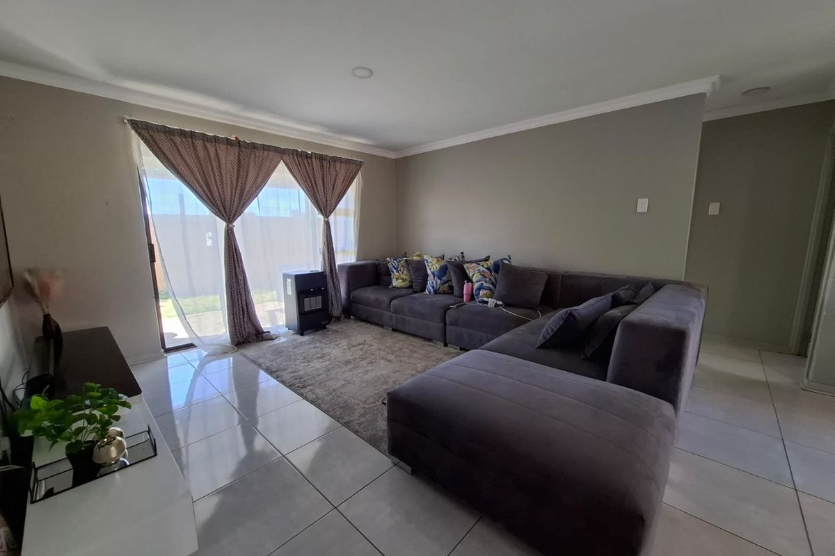 A well-maintained living room featuring large format floor tiles, recessed lighting, and a sliding glass door providing access to the outdoor area.