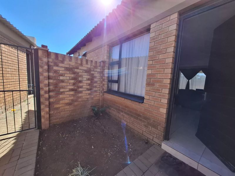 Front entrance area of the townhouse featuring face brick construction, a paved walkway, and a secure metal gate.