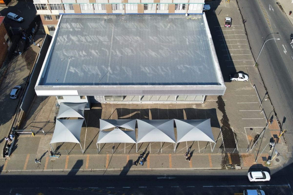 Aerial view of a commercial property featuring a large corrugated metal roof, paved parking area, and multiple shade sail structures.