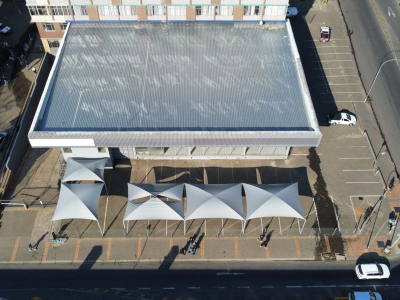 Aerial view of a commercial property featuring a large corrugated metal roof, paved parking area, and multiple shade sail structures.