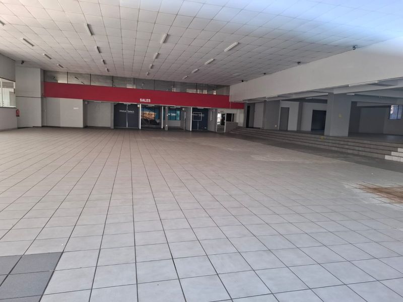 A large, open-plan commercial showroom space featuring tiled flooring, a suspended ceiling with integrated lighting, and a raised platform area.