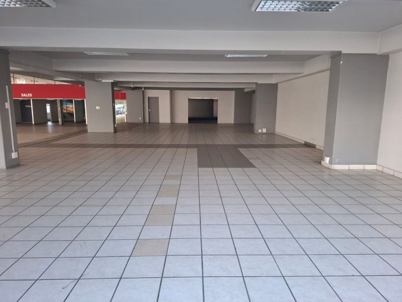 A spacious, vacant open-plan commercial area featuring neutral ceramic tile flooring, structural columns, and recessed ceiling lighting, suitable for various retail or office configurations.