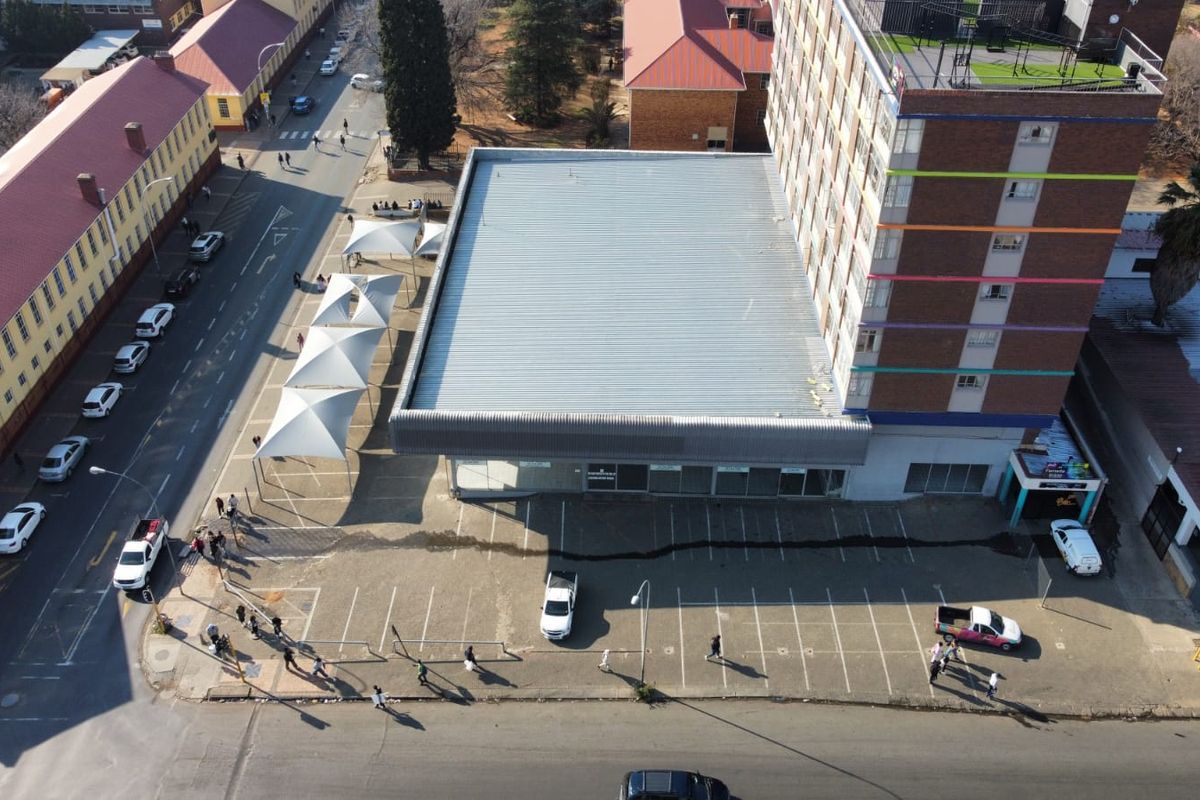 Aerial view of a commercial property featuring a multi-story building, an asphalt parking area, and covered parking bays with tensile shade structures.