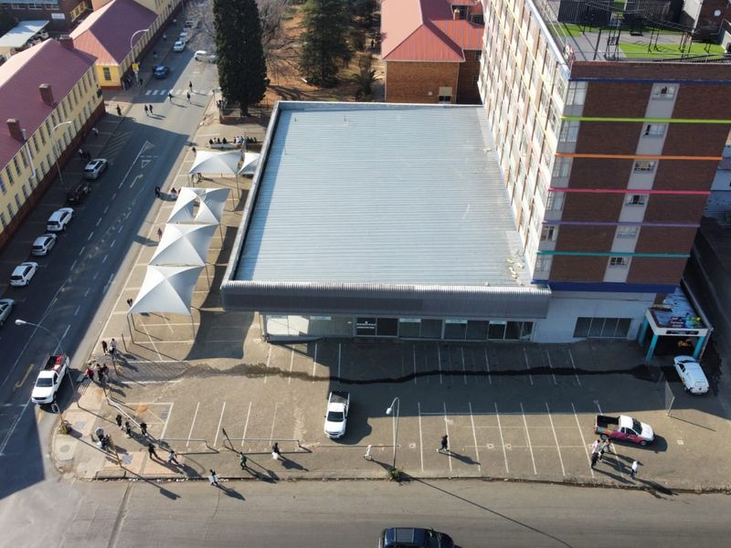 Aerial view of a commercial property featuring a multi-story building, an asphalt parking area, and covered parking bays with tensile shade structures.