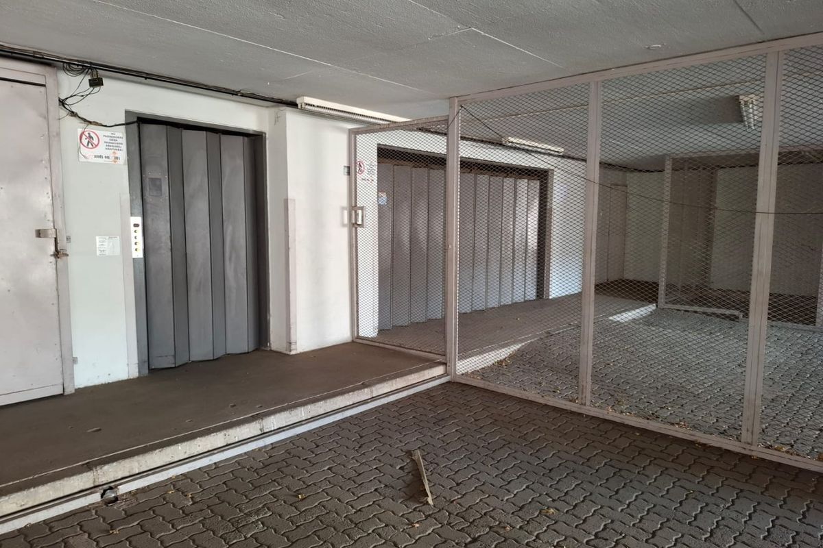 A functional utility area featuring a freight elevator and a secure metal caged storage enclosure with paved flooring.