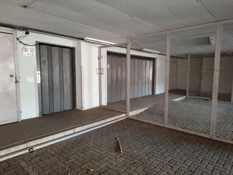 A functional utility area featuring a freight elevator and a secure metal caged storage enclosure with paved flooring.