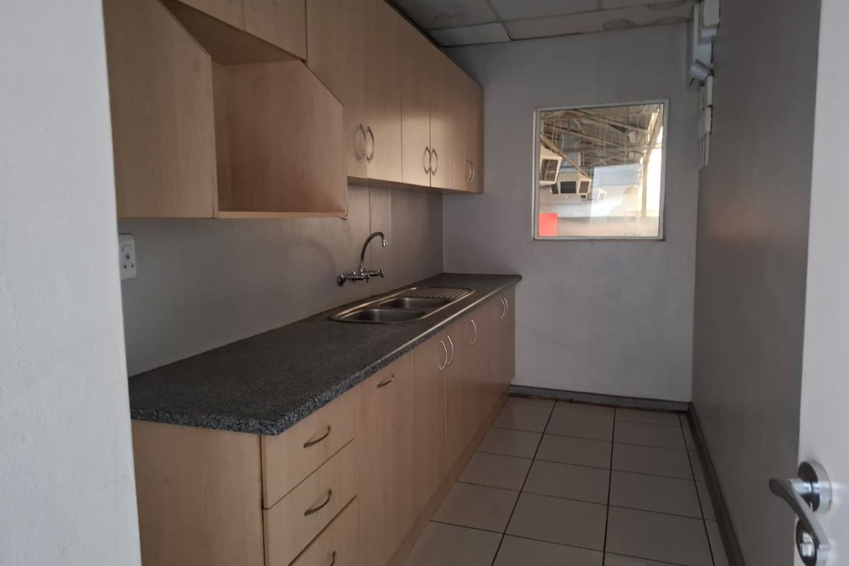 A functional kitchenette featuring laminate cabinetry, granite countertops, a stainless steel double sink, and tiled flooring in a commercial setting.