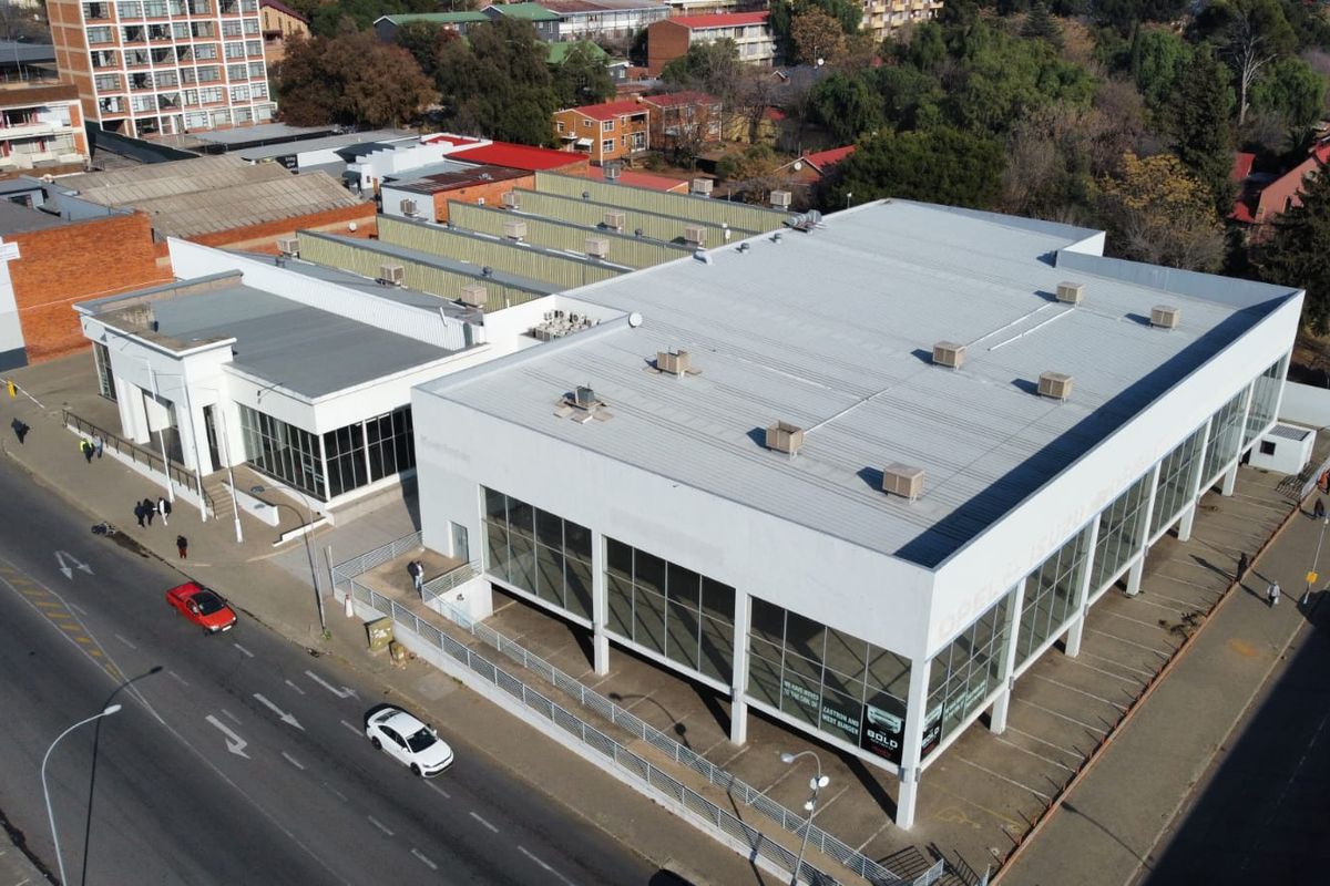 Aerial view of a commercial property featuring a large metal-roofed building with extensive glass frontage and an adjacent paved parking area.