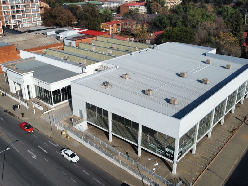 Aerial view of a commercial property featuring a large metal-roofed building with extensive glass frontage and an adjacent paved parking area.
