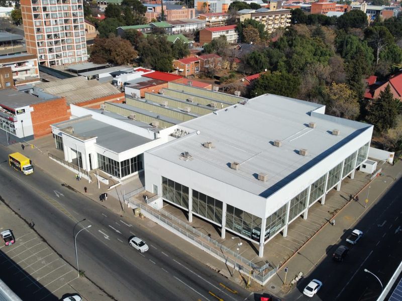 Aerial view of a modern commercial building featuring a large glass facade, metal roofing, and dedicated parking space in an urban setting.