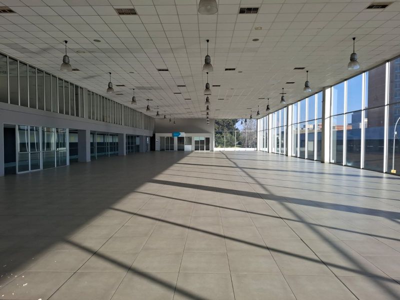 Expansive open-plan commercial space featuring large floor-to-ceiling windows, tiled flooring, and a suspended ceiling with integrated lighting and ventilation.