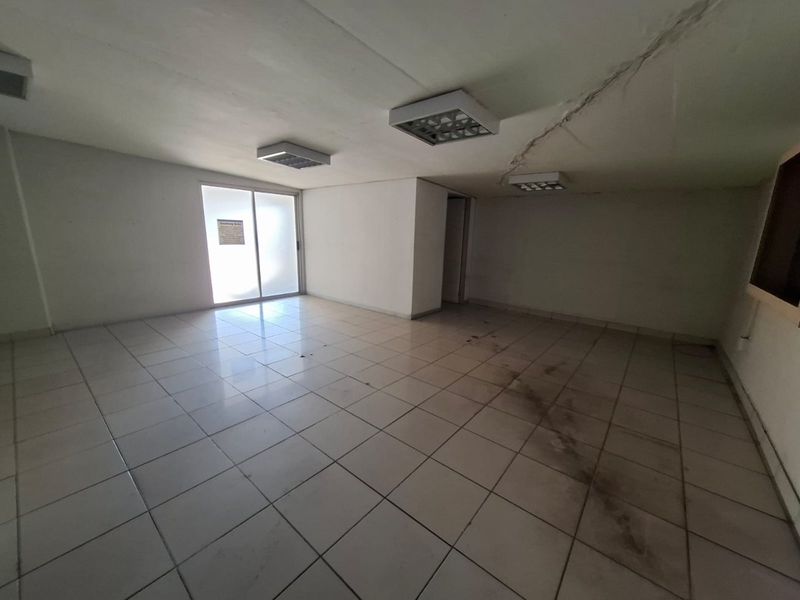 An empty commercial office space featuring ceramic floor tiles, fluorescent lighting, and a sliding glass door, currently showing signs of ceiling cracking and floor staining.