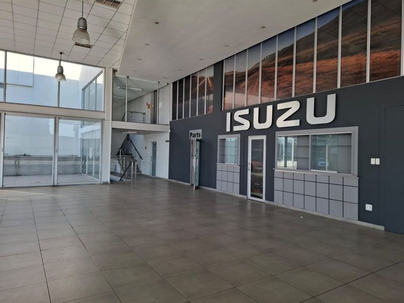Spacious commercial showroom area featuring large glass windows, tiled flooring, a service counter, and an internal staircase leading to an upper level.