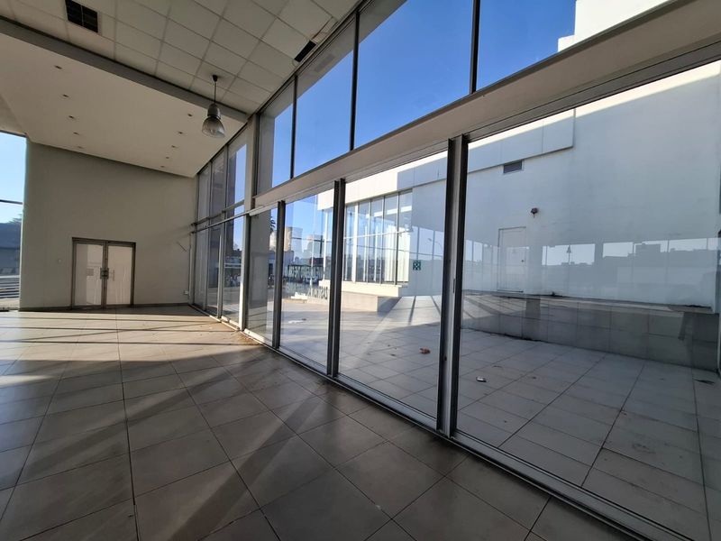 Spacious open-plan commercial area featuring large glass sliding doors, tiled flooring, and a suspended ceiling, offering excellent natural light and access to an outdoor patio.
