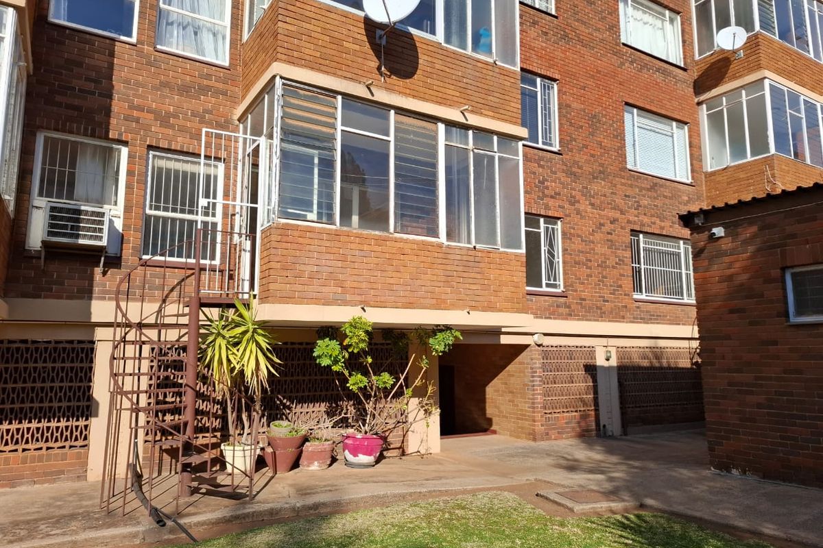 Rear view of a brick apartment building featuring an enclosed balcony, external spiral staircase, and security window bars.
