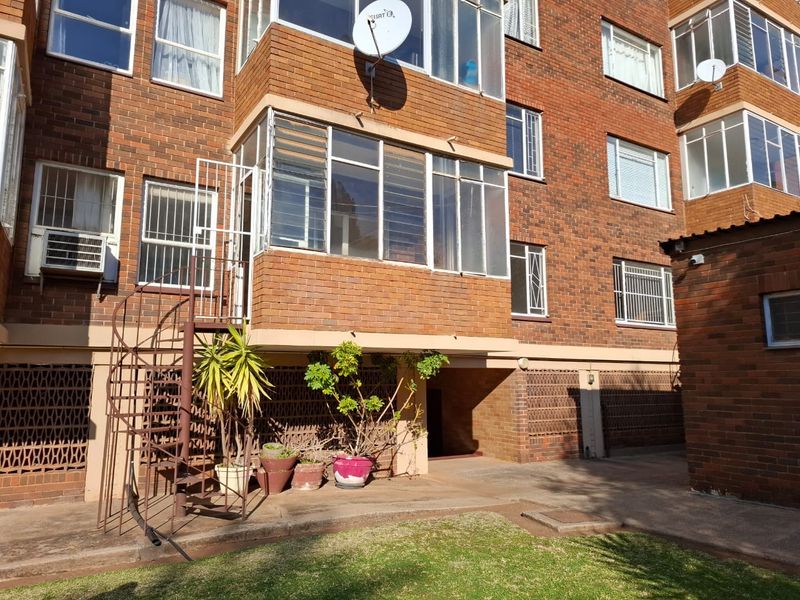Rear view of a brick apartment building featuring an enclosed balcony, external spiral staircase, and security window bars.