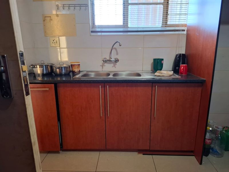 A functional kitchen area featuring a double bowl stainless steel sink, laminate countertops, and built-in wooden cabinetry with a tiled backsplash.