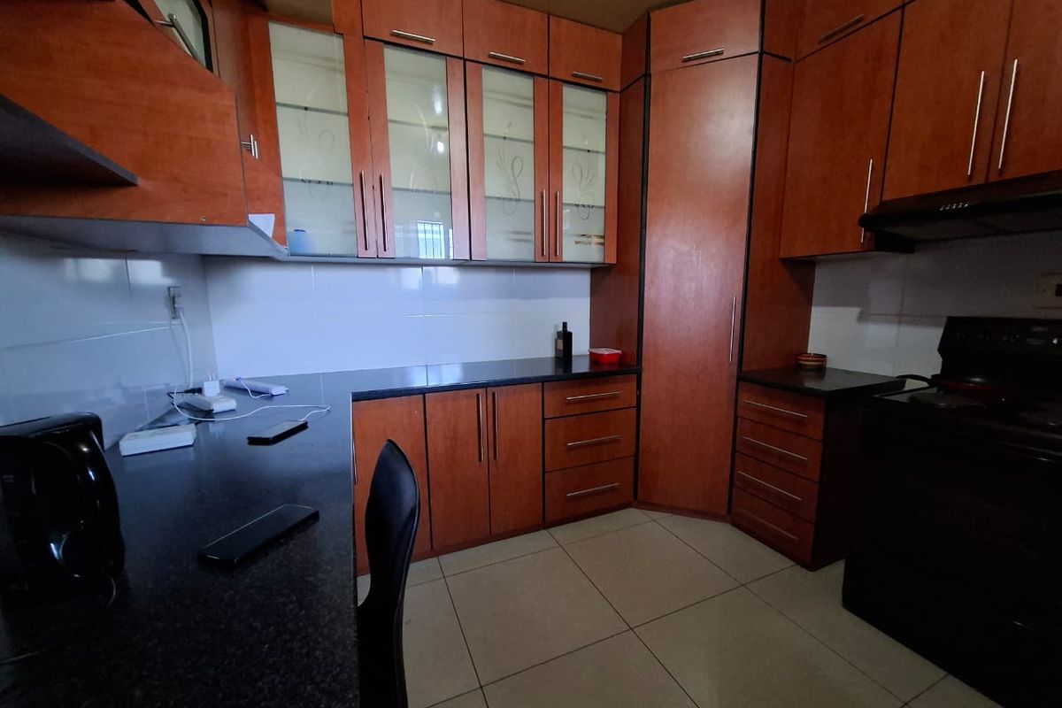 A functional kitchen featuring warm-toned laminate cabinetry, dark granite countertops, and tiled flooring, offering ample storage and workspace.
