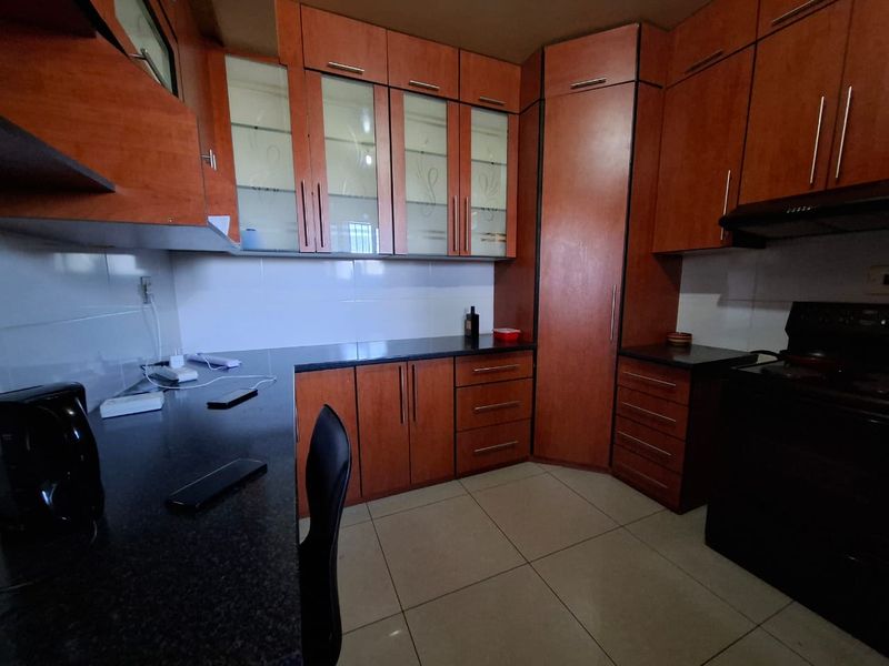 A functional kitchen featuring warm-toned laminate cabinetry, dark granite countertops, and tiled flooring, offering ample storage and workspace.