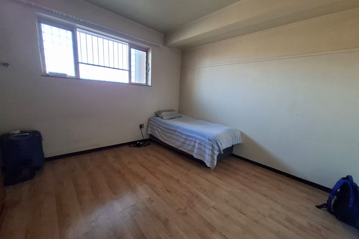 A simple bedroom featuring laminate flooring and a window with security bars, offering a blank canvas for potential interior updates.