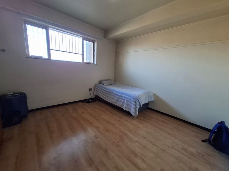 A simple bedroom featuring laminate flooring and a window with security bars, offering a blank canvas for potential interior updates.