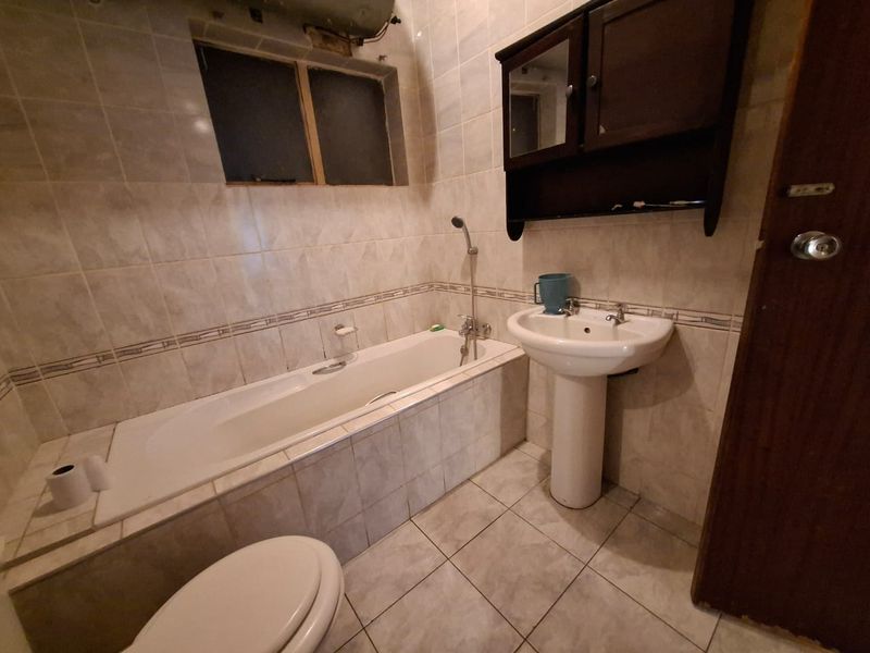 A dated bathroom featuring a built-in bathtub, pedestal basin, and wall-mounted medicine cabinet, finished with neutral wall and floor tiles.