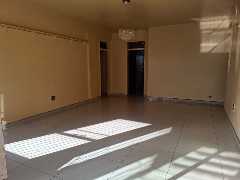 A spacious, empty living area featuring neutral tiled flooring and a decorative crystal chandelier, offering a blank canvas for interior design.