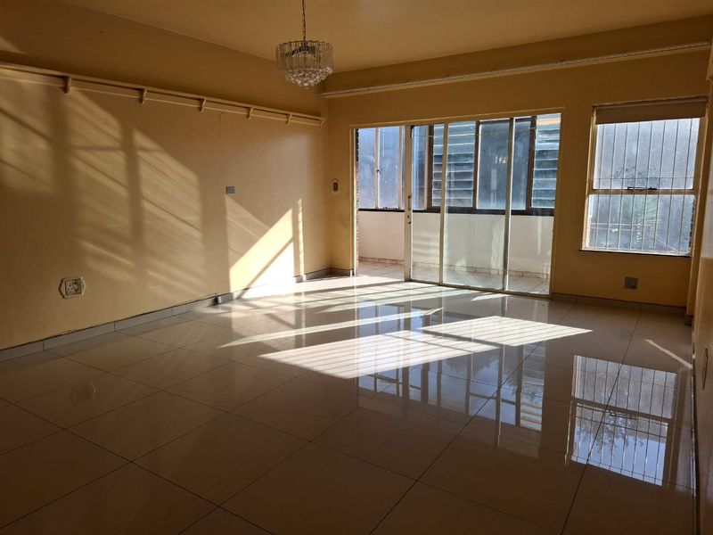 Spacious, sunlit living area featuring polished tiled flooring, a ceiling light fixture, and direct access to an enclosed balcony through sliding glass doors.