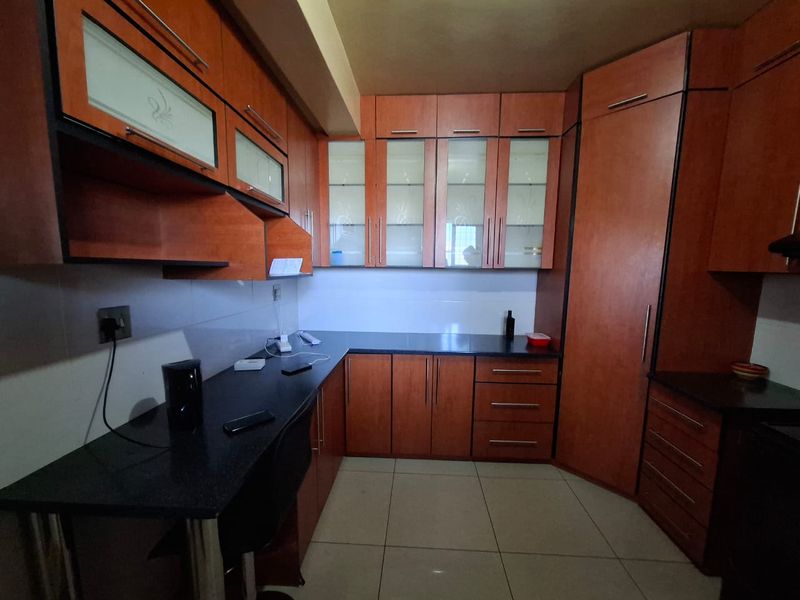 A functional kitchen featuring dark granite countertops, extensive wood-finish cabinetry with glass-fronted upper units, and neutral floor tiles.