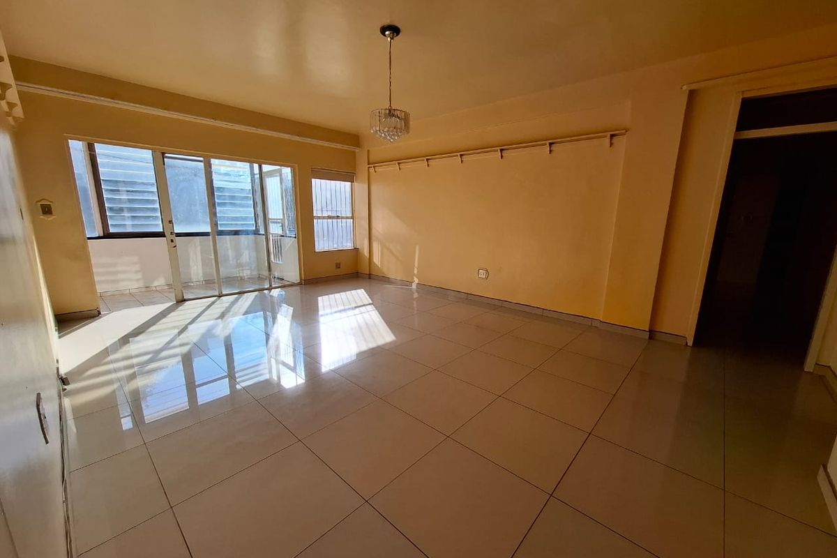 A spacious, empty living room featuring large format floor tiles, sliding glass doors leading to a balcony, and neutral wall finishes.