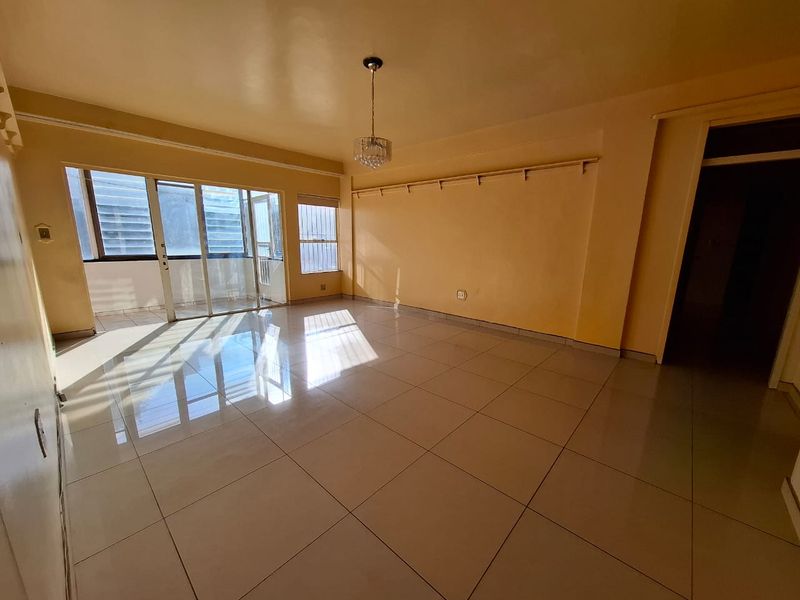 A spacious, empty living room featuring large format floor tiles, sliding glass doors leading to a balcony, and neutral wall finishes.