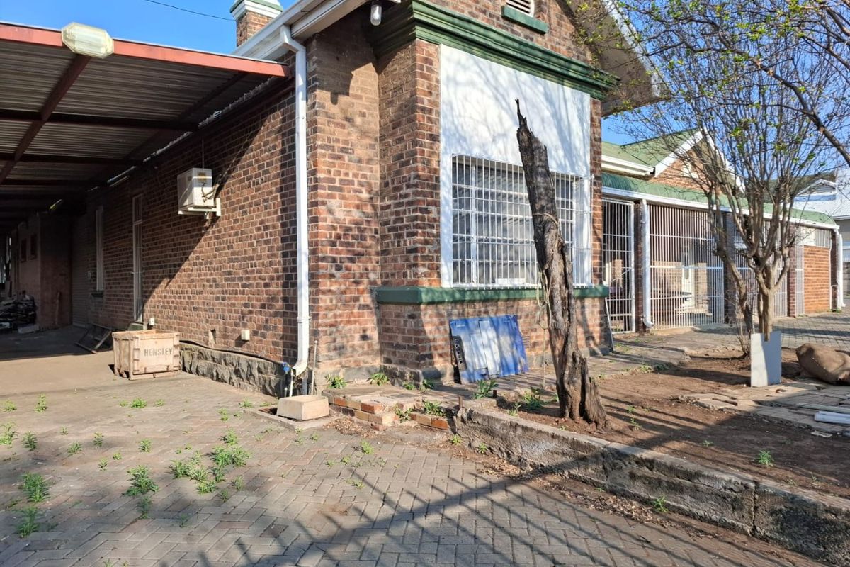 Rear exterior view of a brick commercial building featuring a carport, security bars on windows, and a paved area requiring maintenance.