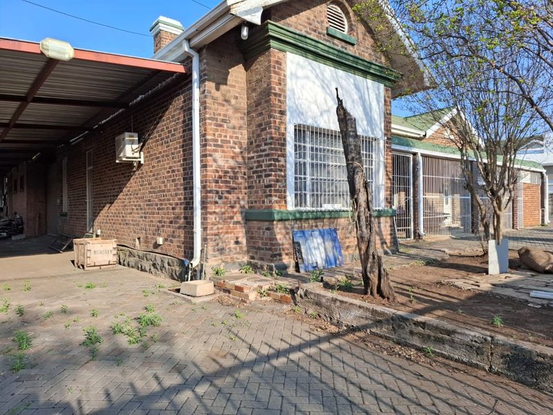 Rear exterior view of a brick commercial building featuring a carport, security bars on windows, and a paved area requiring maintenance.