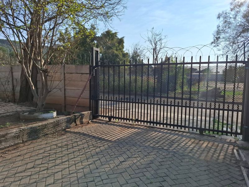 A secure commercial property entrance featuring a black metal sliding gate, perimeter wall with razor wire, and a paved driveway.
