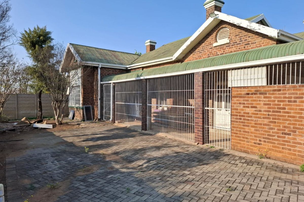 Rear exterior view of a brick commercial building featuring a paved courtyard, corrugated metal roofing, and secure metal grille enclosures.