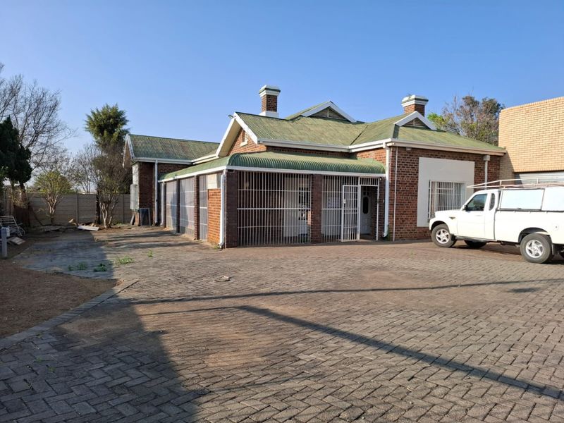 Front view of a commercial brick building featuring a corrugated metal roof, security bars on windows and doors, and a paved driveway area.