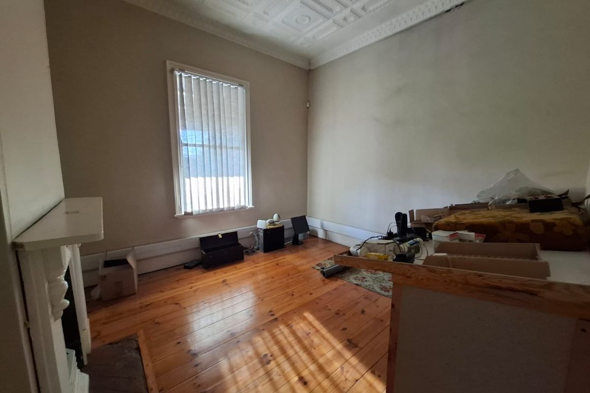 A vacant living room featuring original timber flooring, an ornate pressed metal ceiling, and a fireplace mantel, requiring cosmetic updates to walls and flooring.
