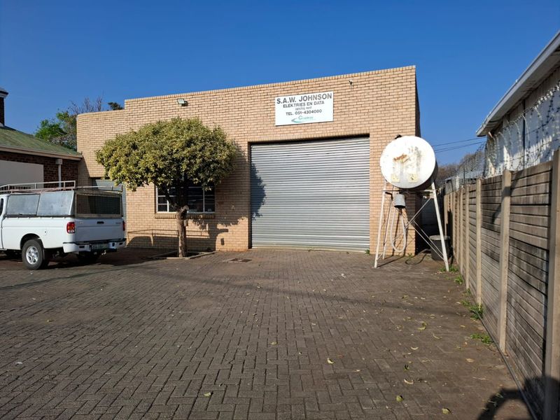 Commercial warehouse exterior featuring a brick facade, large roller shutter door, paved driveway, and an elevated water tank.