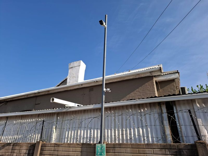Exterior view of a commercial property featuring a brick boundary wall with razor wire, security cameras, and corrugated metal wall cladding.