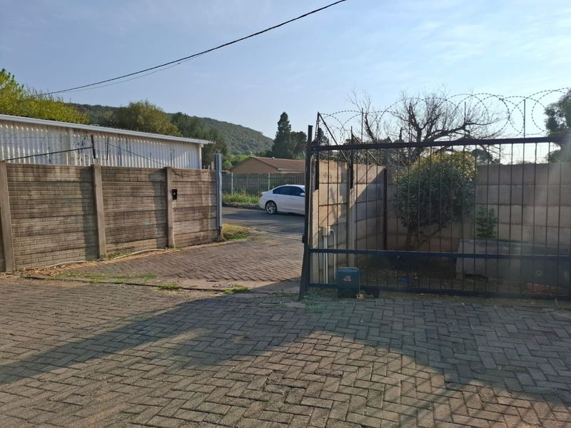 Front entrance area featuring a paved driveway, precast concrete boundary wall, and a metal security gate with razor wire.