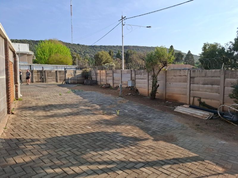 Rear exterior area featuring a paved surface, enclosed by a precast concrete boundary wall with security razor wire.