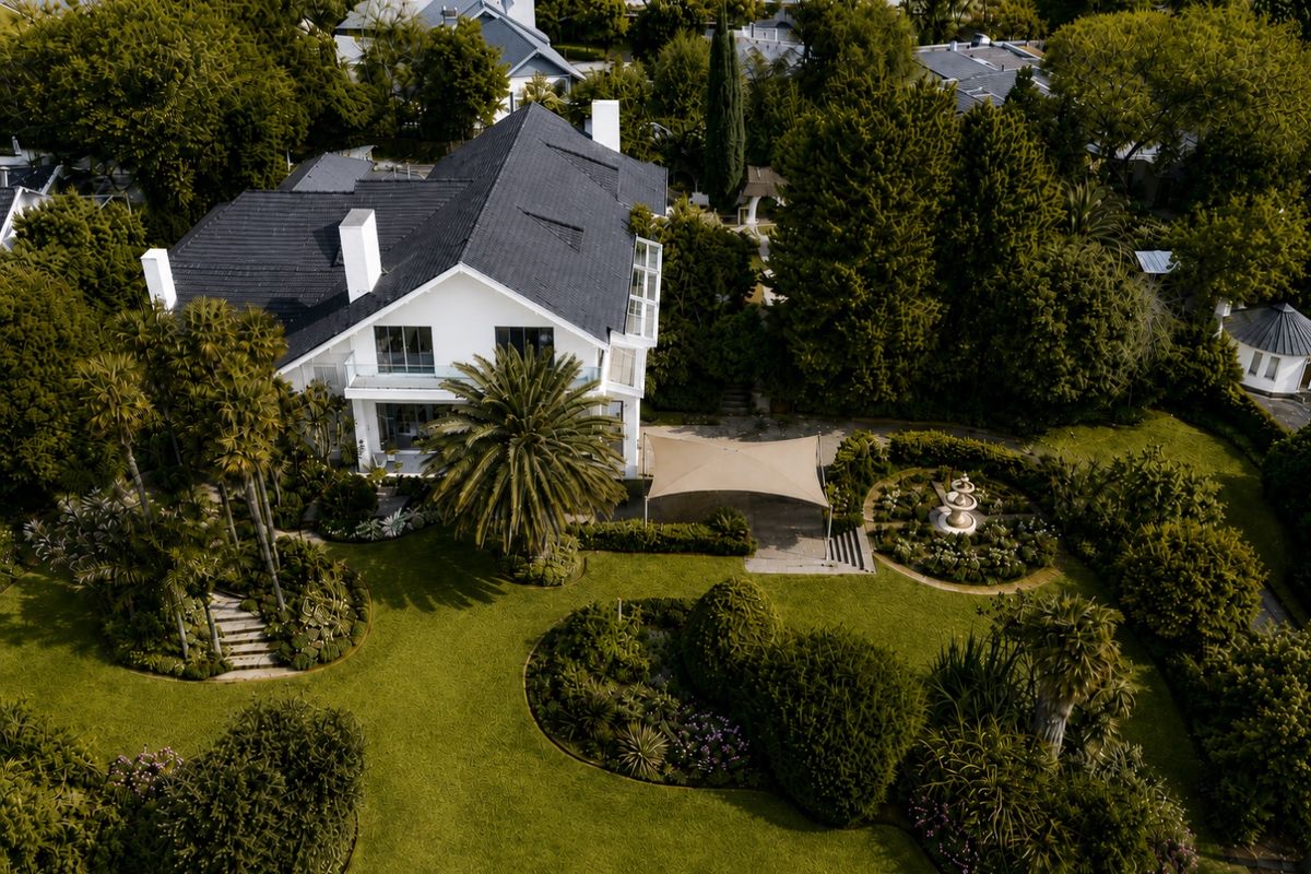 Aerial view of a well-maintained residential property featuring a large landscaped garden, stone fountain, shade sail, and a multi-level house with a tiled roof.