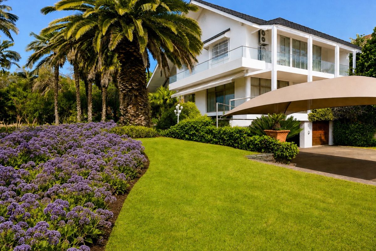 A well-maintained rear exterior view of a multi-story home featuring a landscaped garden, glass balustrades, and a paved driveway area.