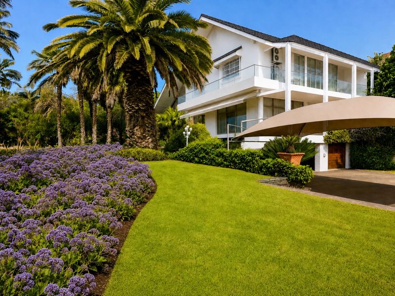 A well-maintained rear exterior view of a multi-story home featuring a landscaped garden, glass balustrades, and a paved driveway area.