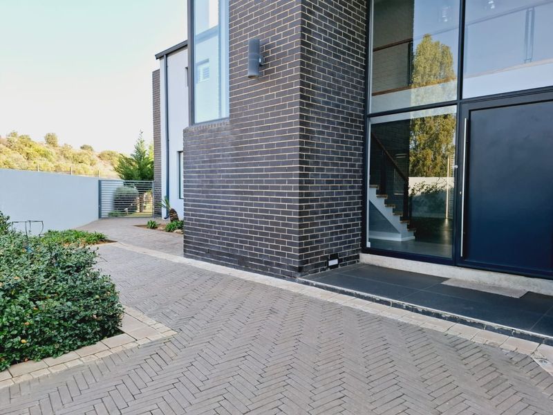 Modern architectural front facade featuring dark brickwork, expansive glass windows, and a neatly paved herringbone driveway leading to the entrance.