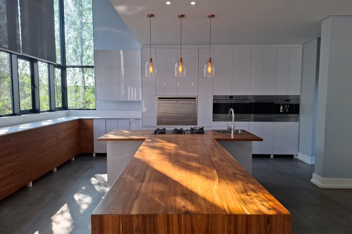 Modern kitchen featuring a large timber-topped island, high-end built-in appliances, floor-to-ceiling cabinetry, and expansive windows providing ample natural light.