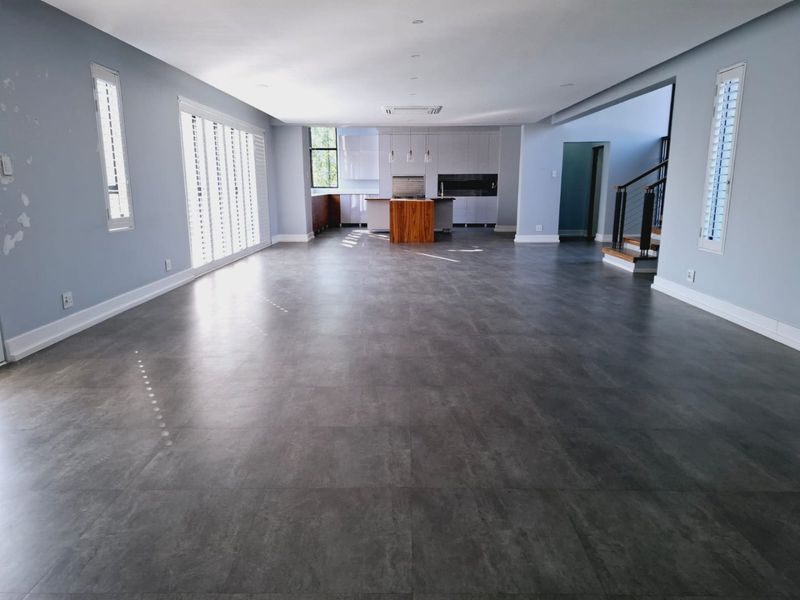 Spacious open-plan living area featuring large format floor tiles, a modern kitchen with island, and a staircase, offering a bright and versatile layout.