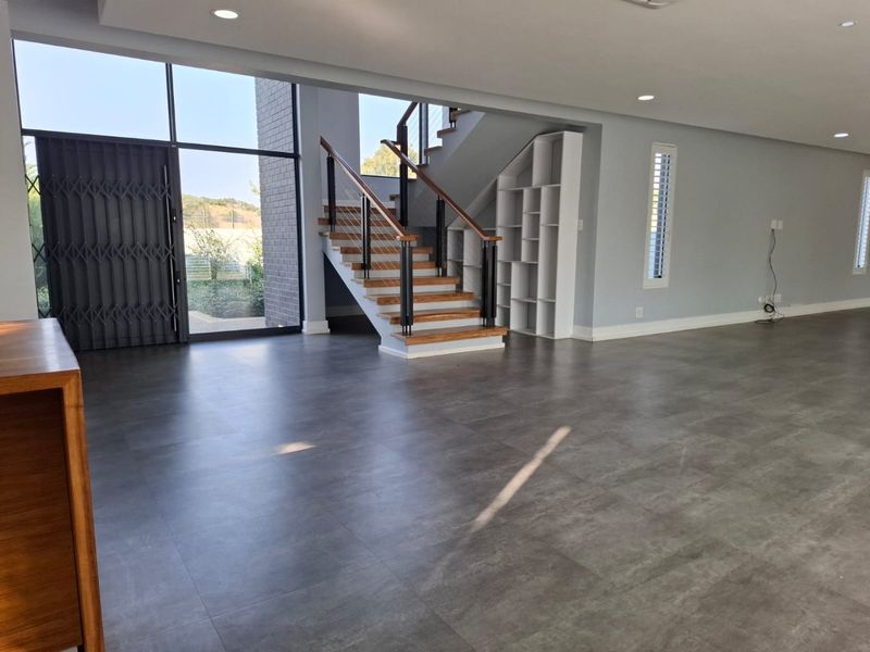 Spacious open-plan living area featuring modern tiled flooring, a contemporary staircase with wooden treads, and large windows providing ample natural light.
