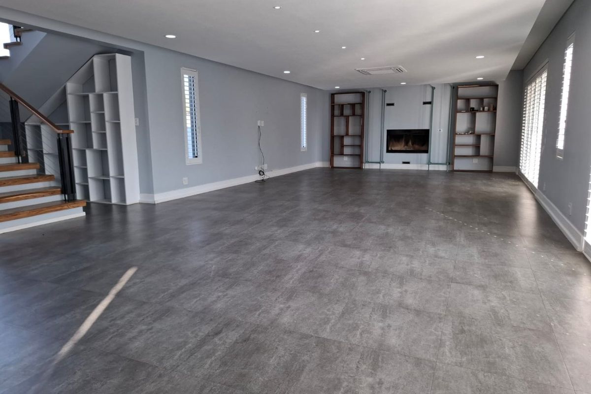 Spacious open-plan living area featuring large format floor tiles, a built-in fireplace, integrated shelving, and a modern staircase with wooden treads.